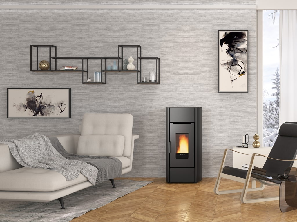 Piec na pellet La Nordica Mirka Plus w eleganckiej, czarnej obudowie z dużym przeszkleniem frontowym, przez które widać migoczące płomienie. Urządzenie stoi w nowoczesnym salonie z jasnymi ścianami i drewnianą podłogą. W tle znajduje się minimalistyczna aranżacja wnętrza, w tym wygodna sofa i stylowe dekoracje, tworzące przytulną i harmonijną przestrzeń.